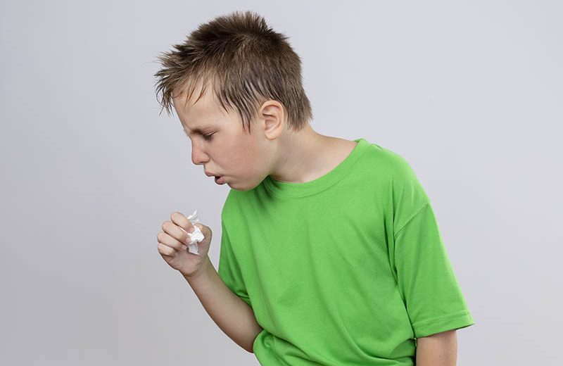 ill little boy green t shirt feeling unwell coughing standing white wall Prapatsorn Medical เครื่องมือกายภาพบำบัด และตรวจปอด